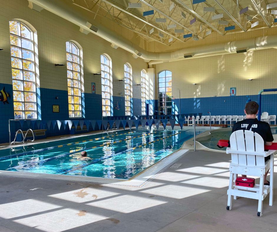 A photo taken of the lap pool from behind the lifeguard's chair. A man swims down the second lane