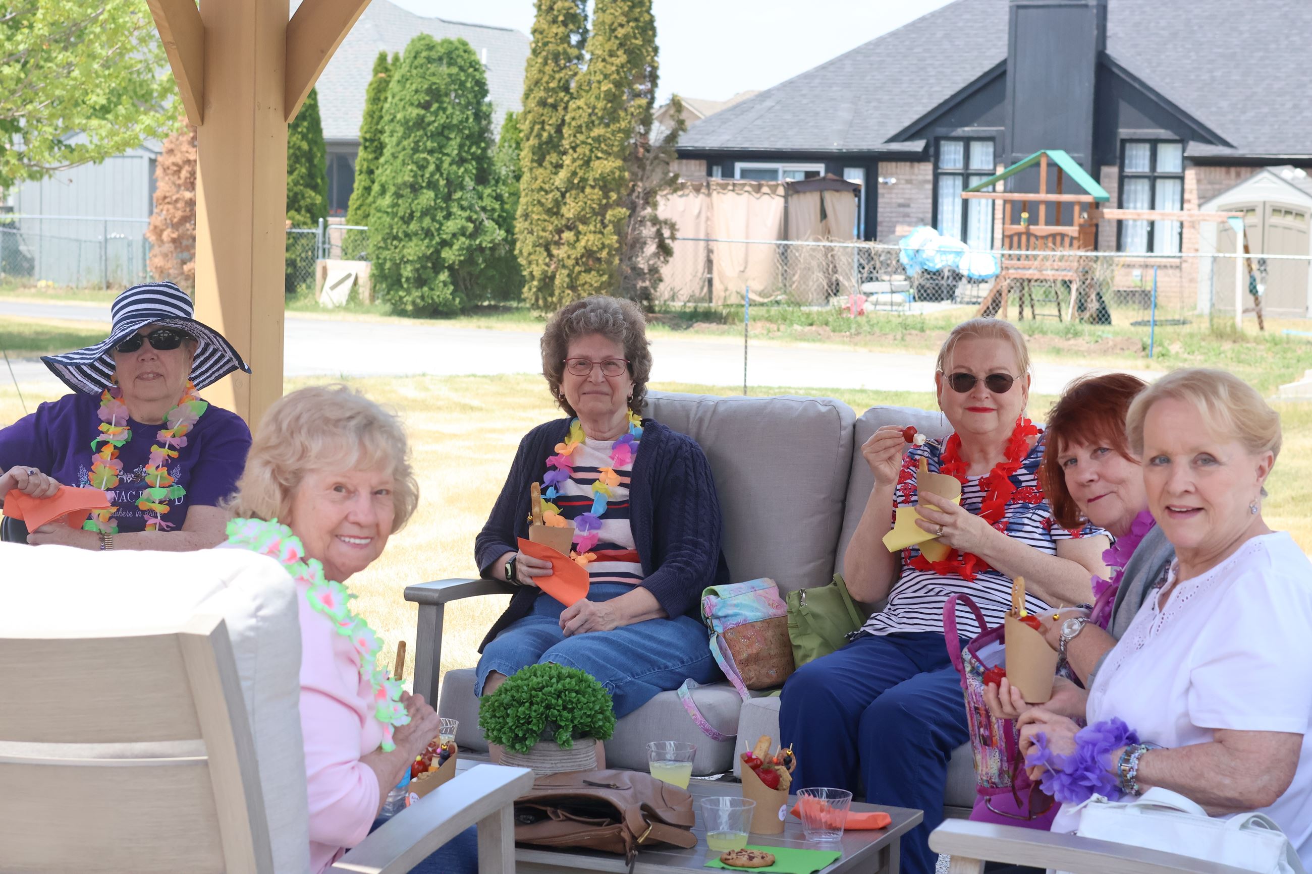 Six seniors sitting outside under a gazebo smiling holding charcuterie cups.