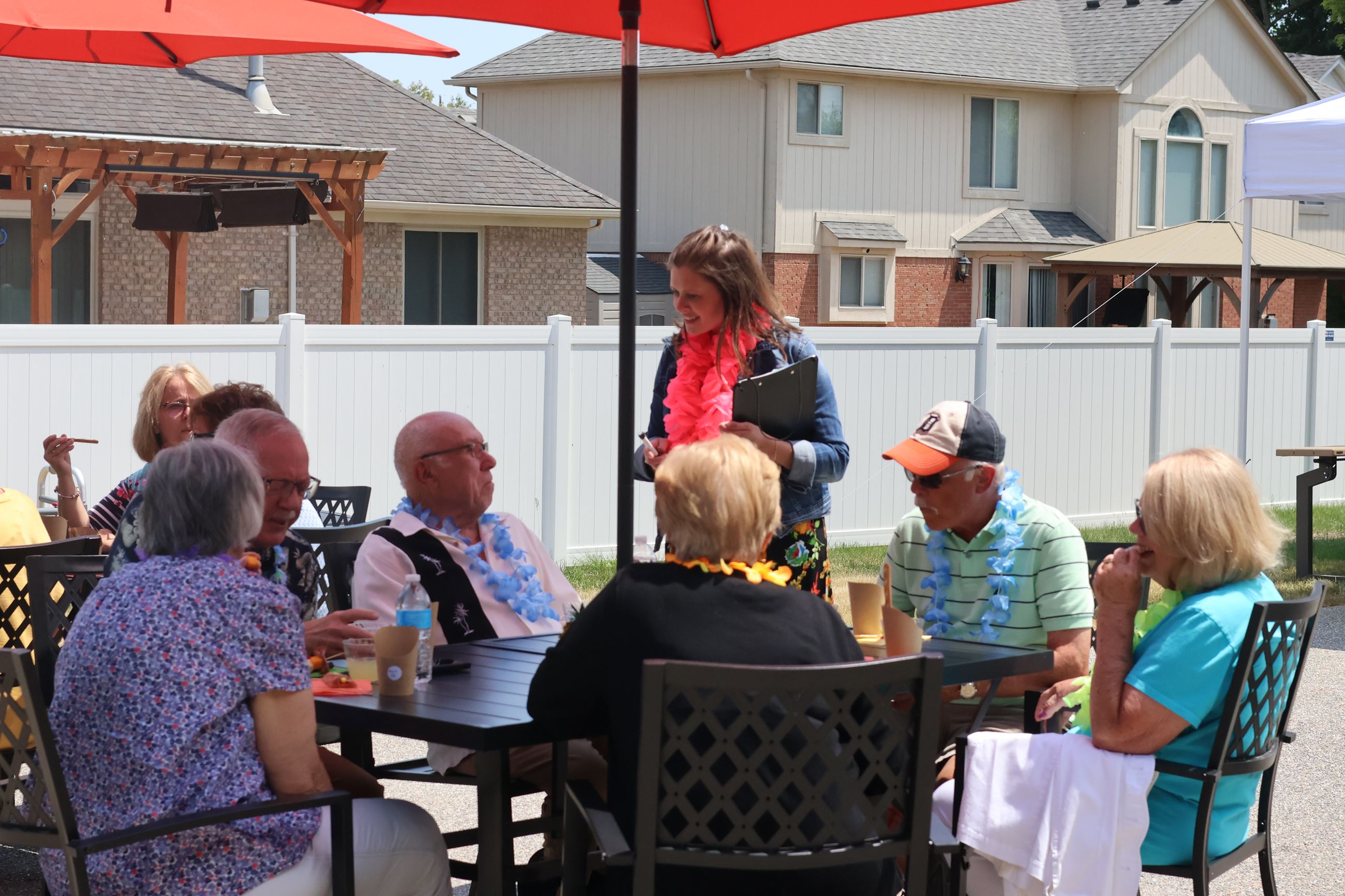 Six seniors sitting at an outside table on the back patio talking to the Senior Coordinator.