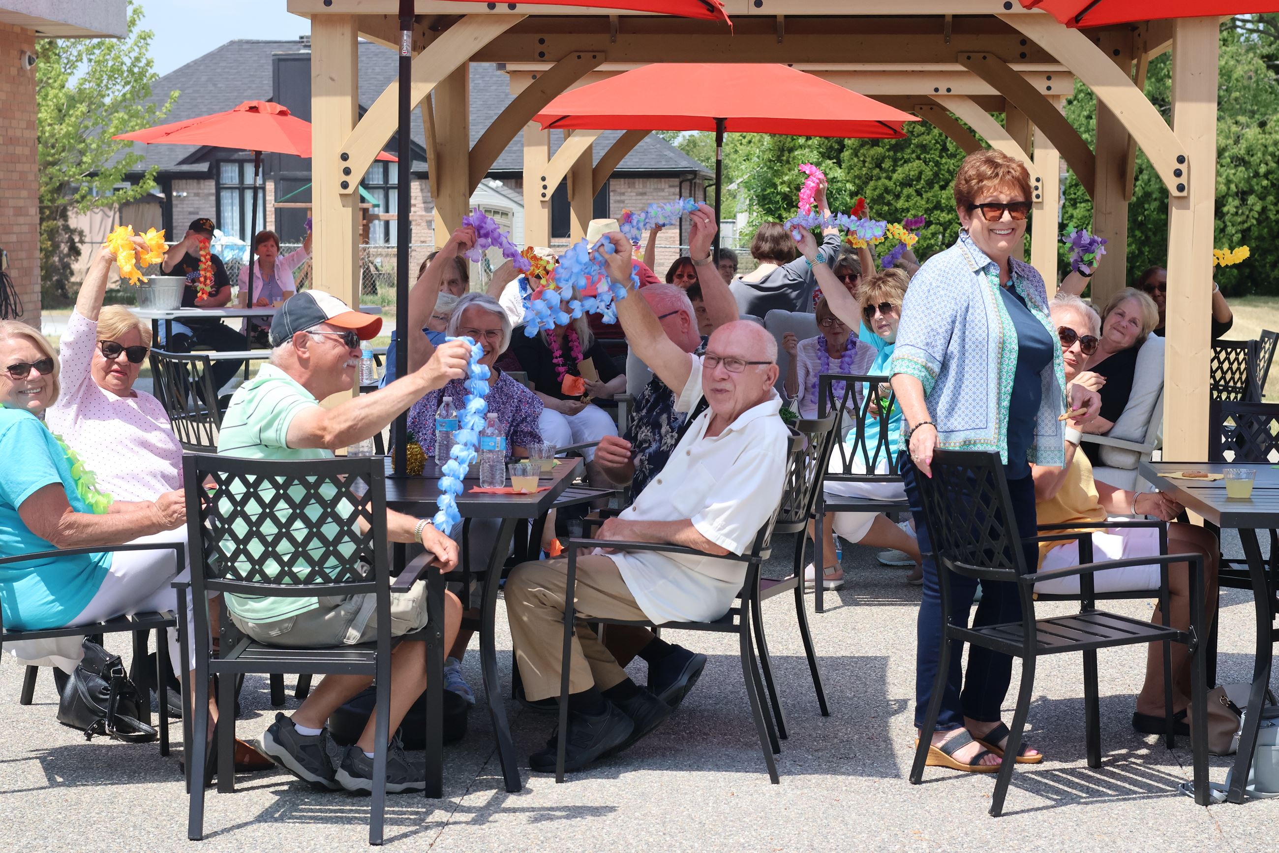 Group of Seniors smiling and waving Hawaiian leis on the senior center patio.