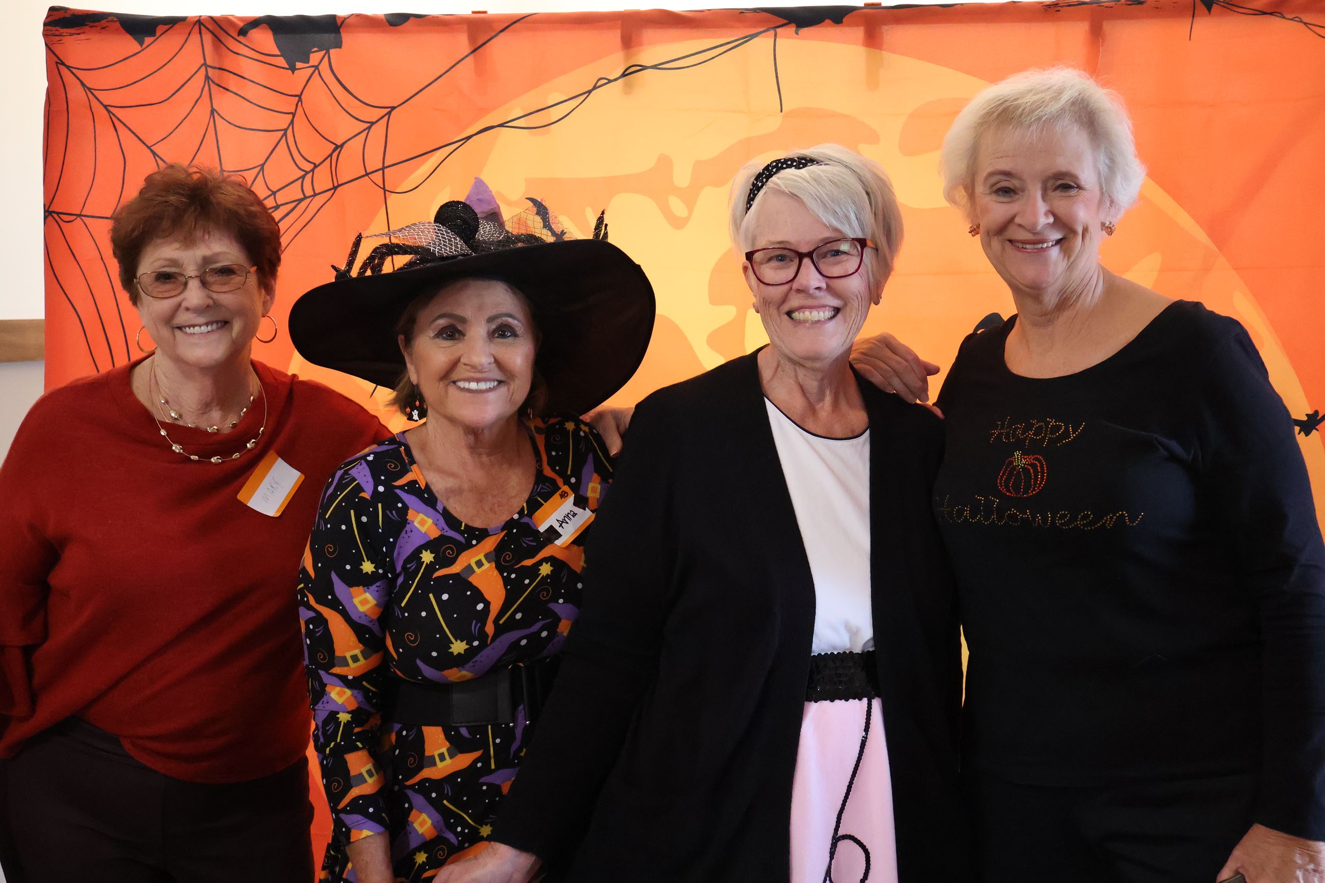 Four Seniors smiling in front of an orange Halloween banner. 