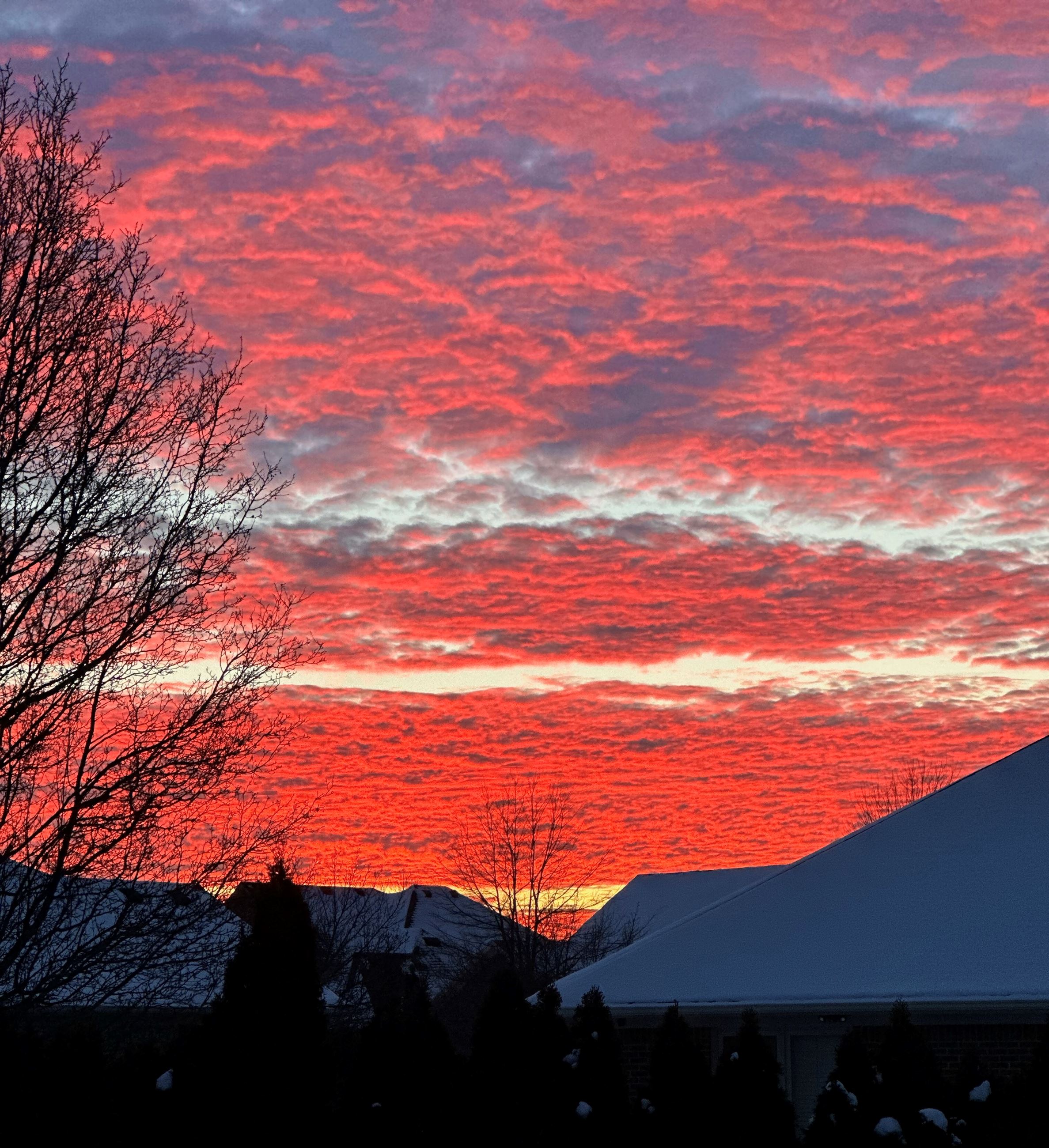 A bright orange and pink sunrise peek through dense clouds captured above snow-capped homes.