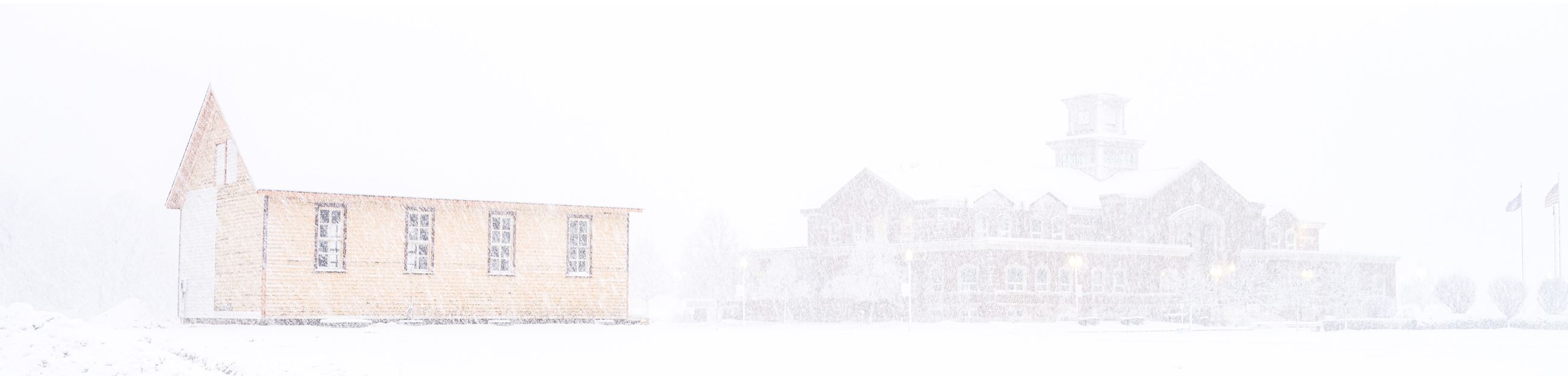 Historic Township Hall in a blizzard with current Township Hall in the distance beyond the snow.